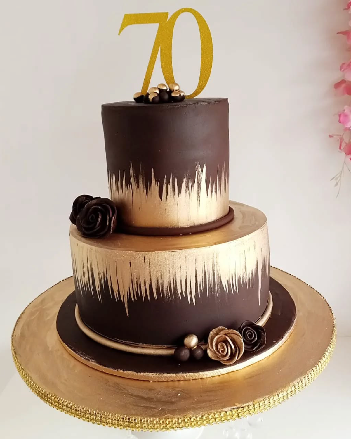 Two-tiered chocolate cake with gold accents and a '70' topper on a white background.