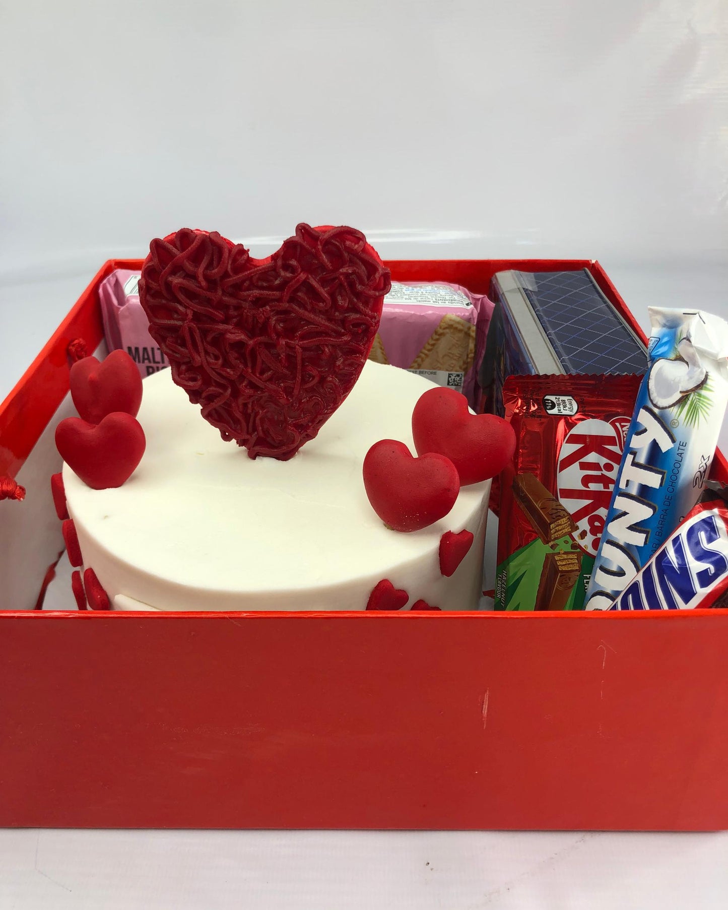 Red heart-shaped gift box with a cake, candy, and snacks on a white background