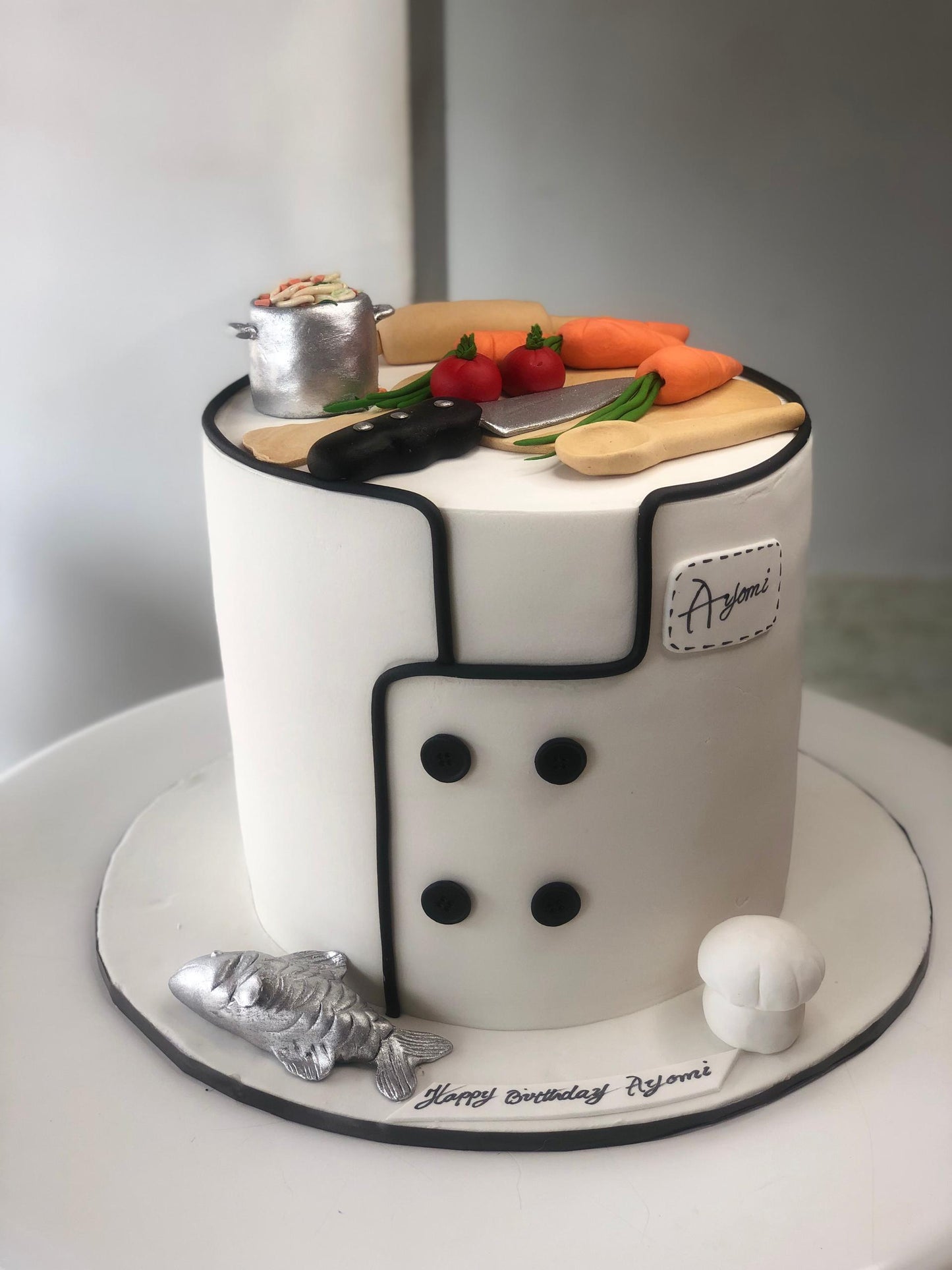 Cake designed to resemble a chef's uniform with kitchen utensils and ingredients on a white background