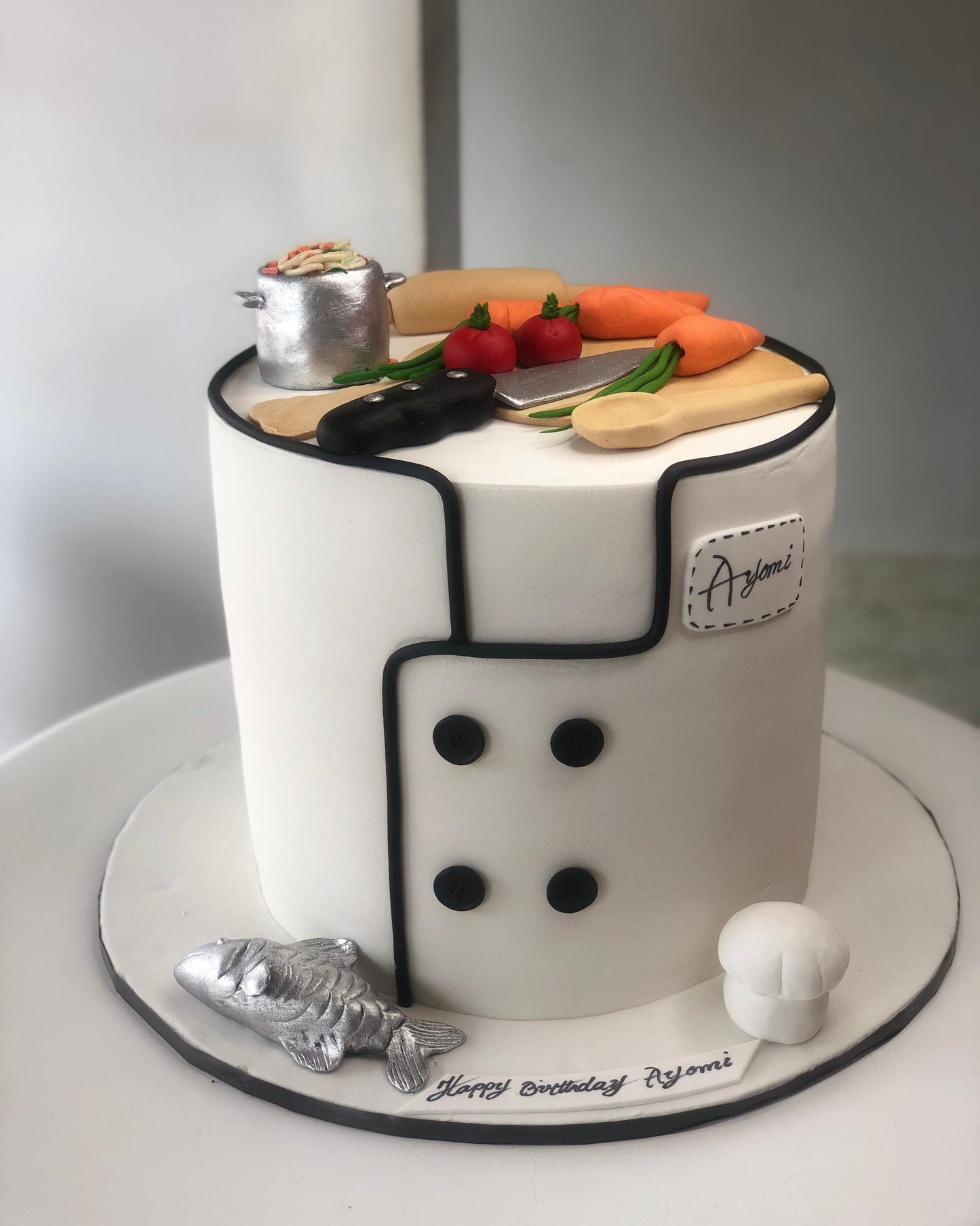 Cake designed to resemble a chef's uniform with kitchen utensils and ingredients on a white background