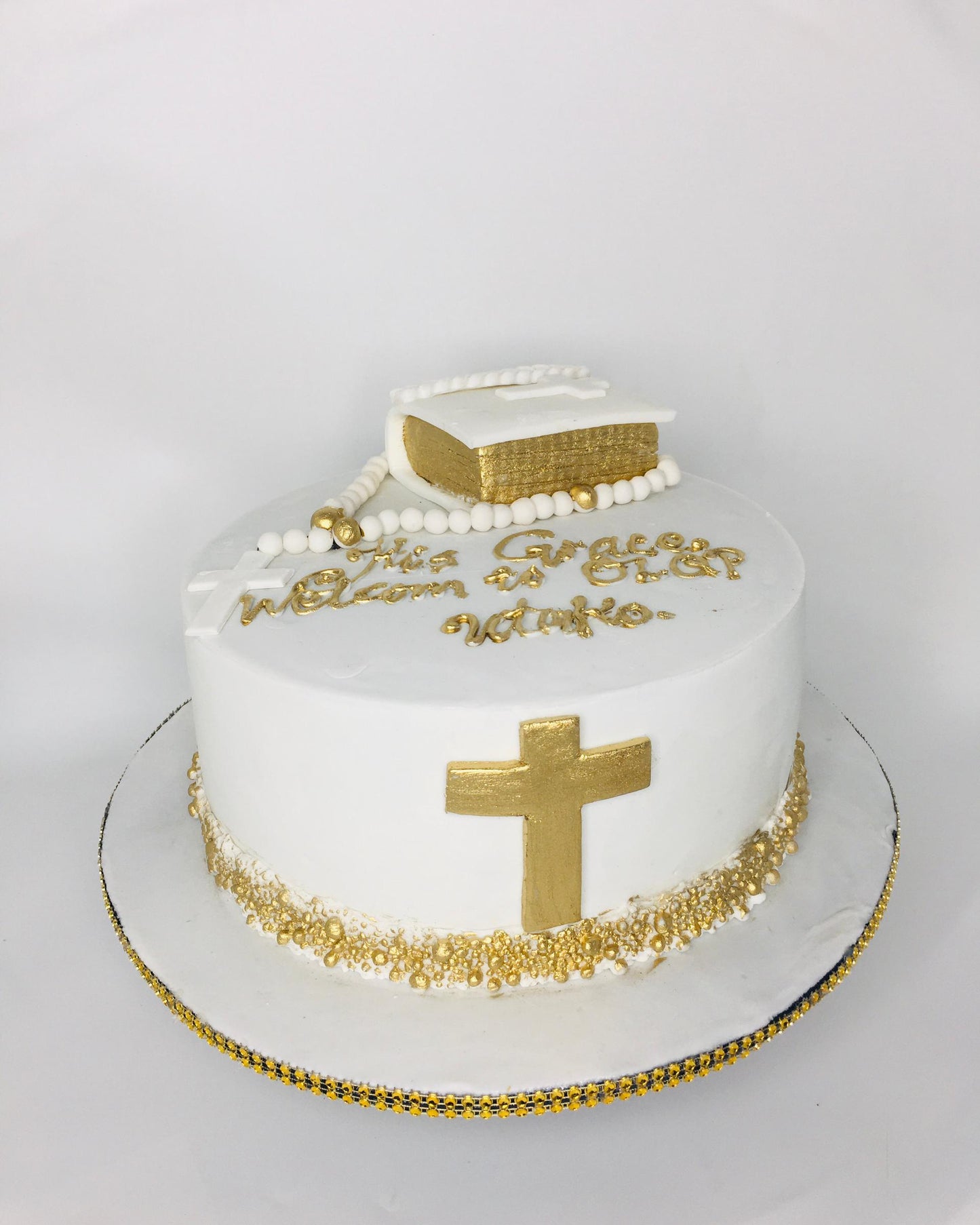 White cake with gold cross, beads, and Bible on a white background
