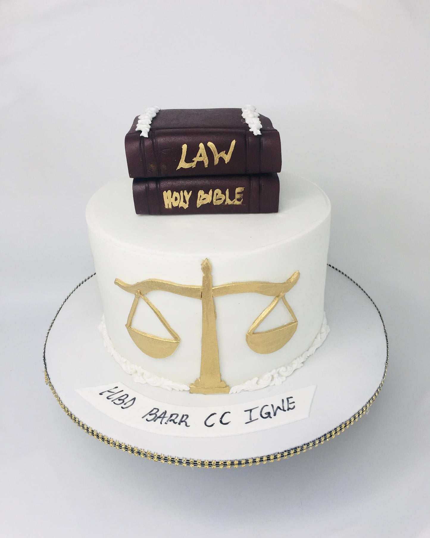 Cake with books labeled 'Law' and 'Holy Bible', scales of justice, and text on a white background