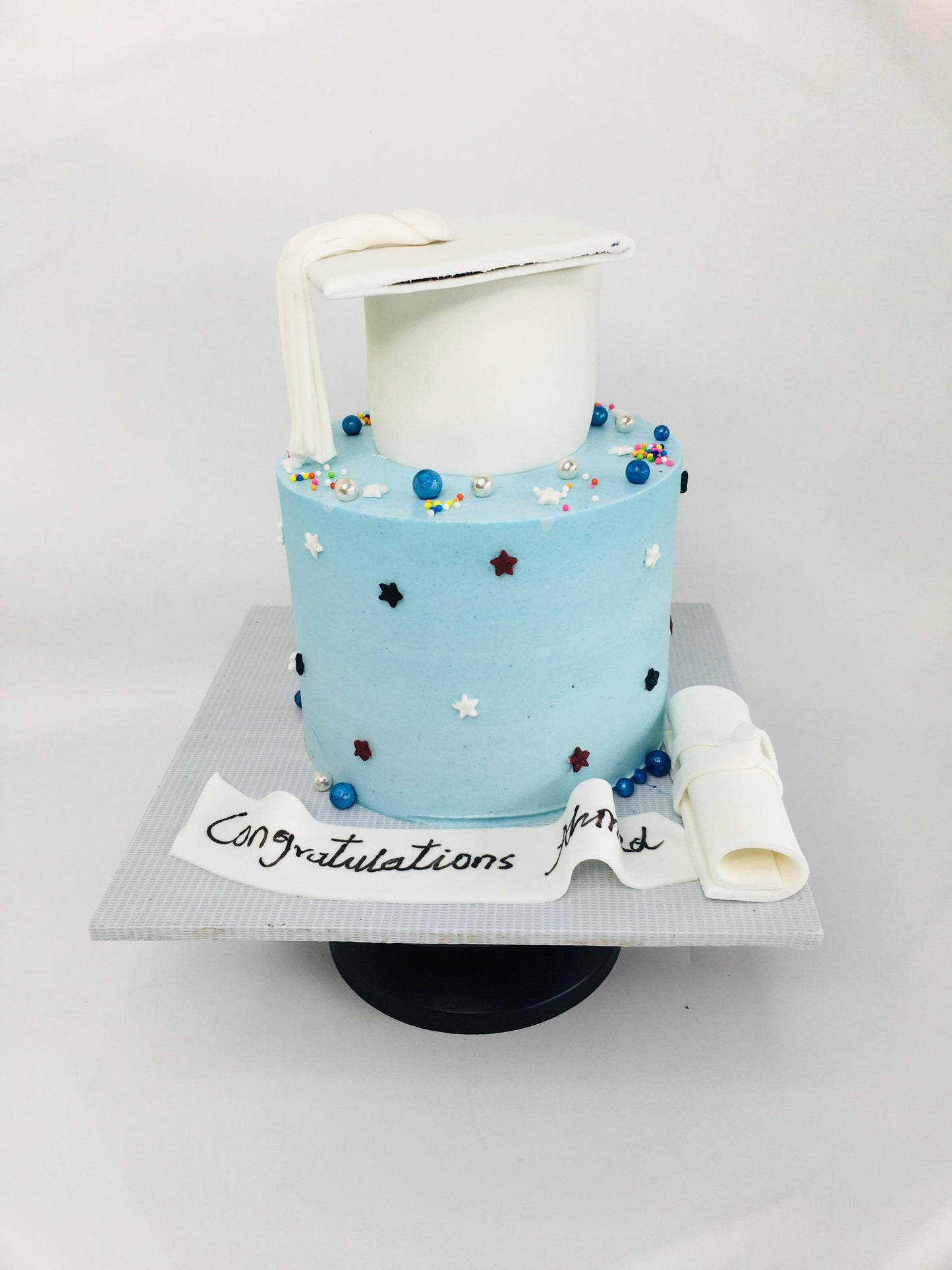 Graduation-themed cake with blue frosting, white diploma, and colorful decorations on a white background