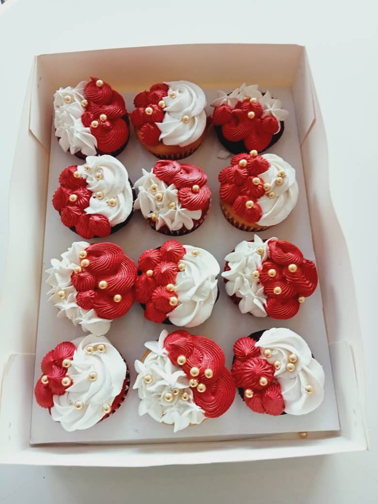 Box of cupcakes with red and white frosting in a decorative pattern.