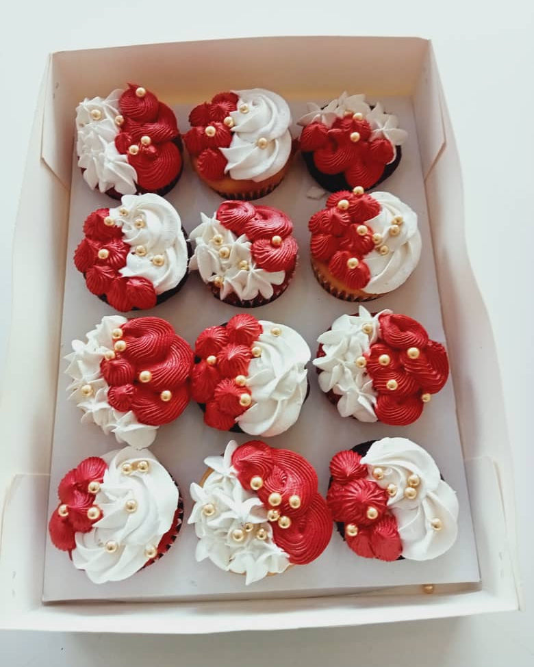 Box of cupcakes with red and white frosting in a decorative pattern.