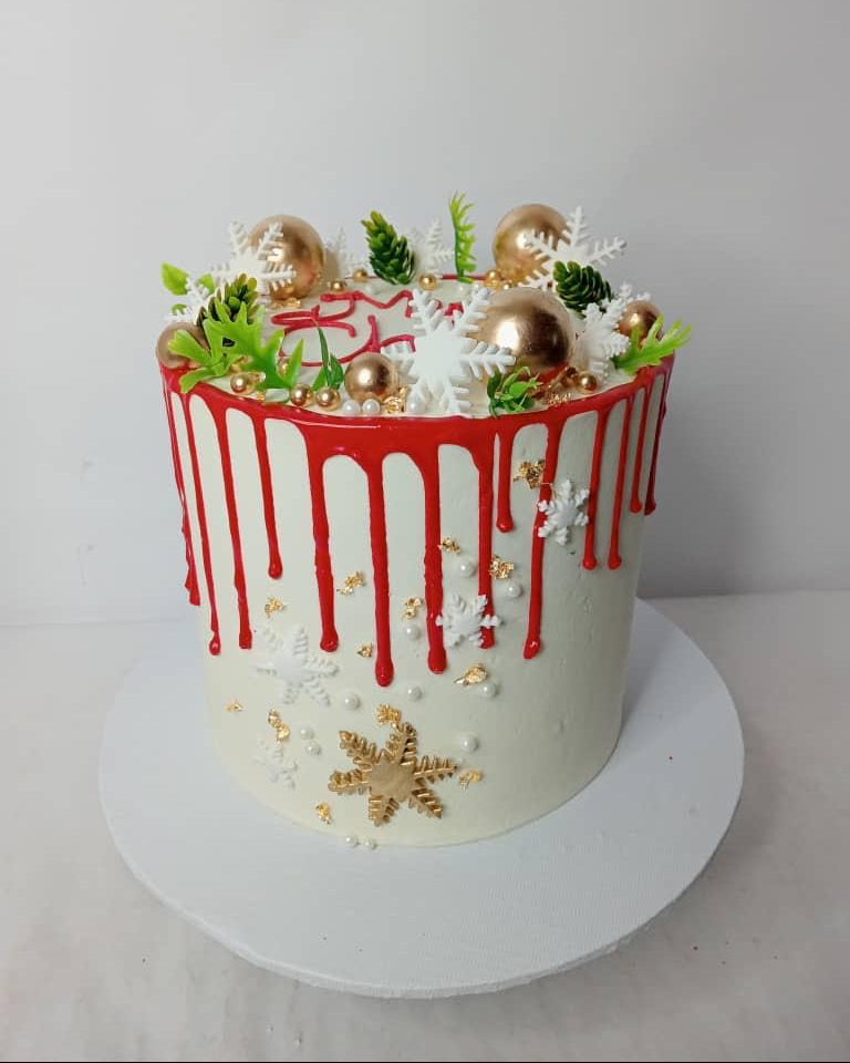 Decorative cake with red drizzle, gold balls, and greenery on a white background