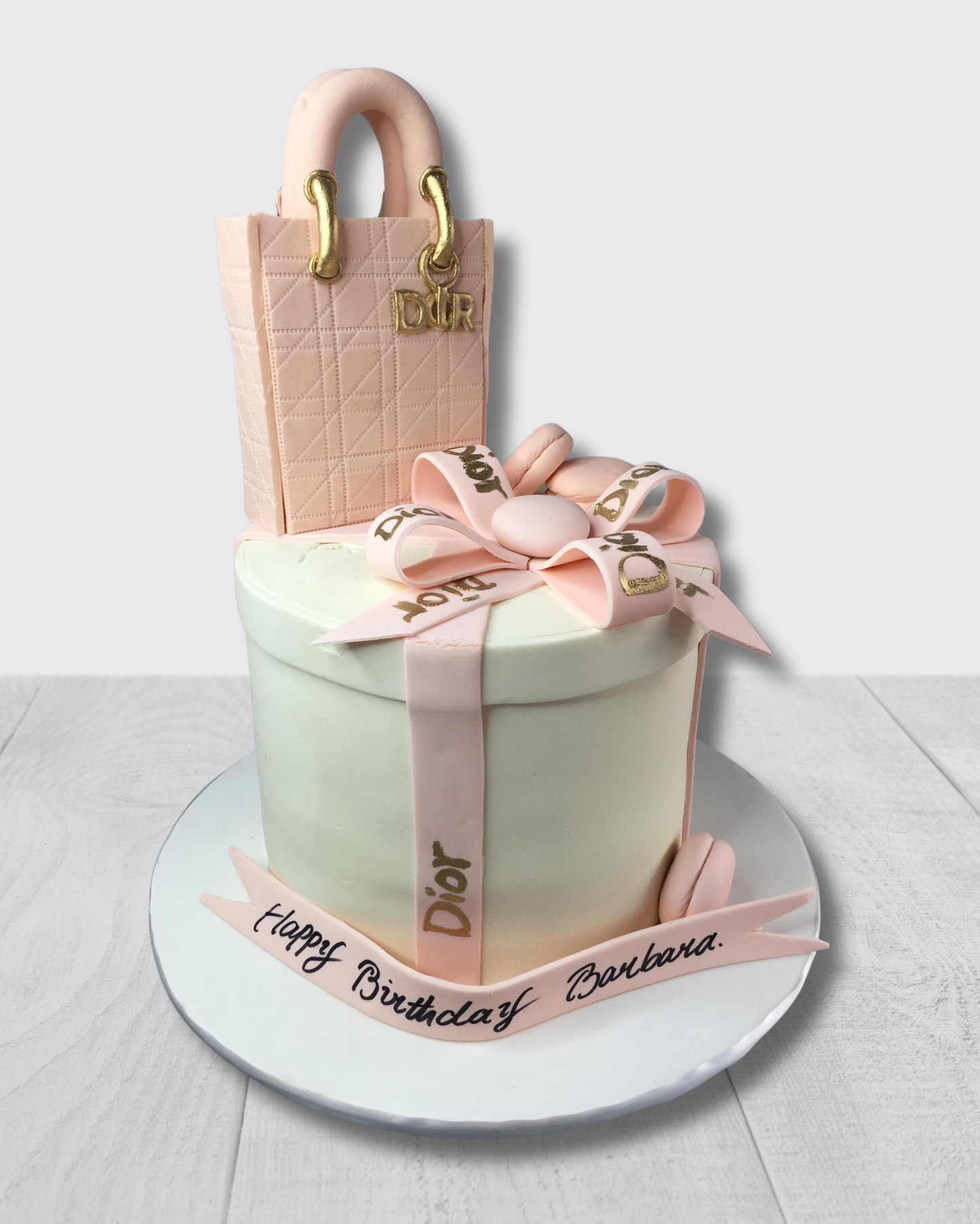 Cake designed like a Dior handbag with ribbons and text on a white background