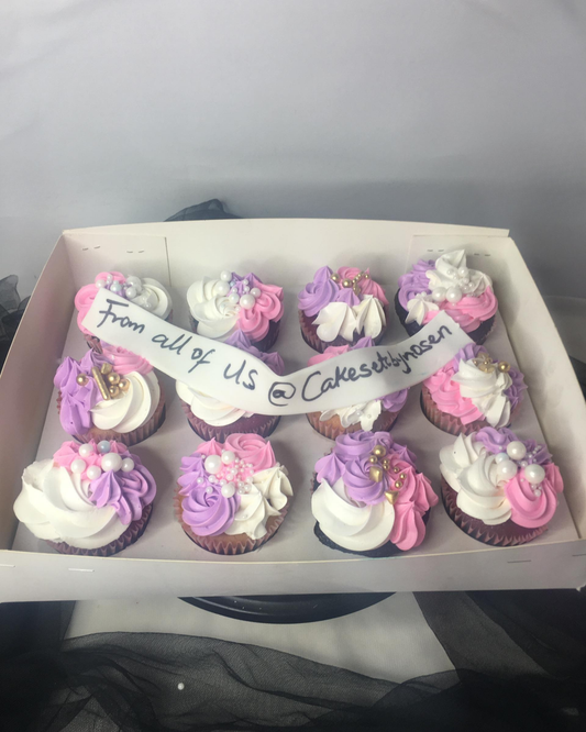 Box of cupcakes with pink, purple, and white frosting, featuring a handwritten message.