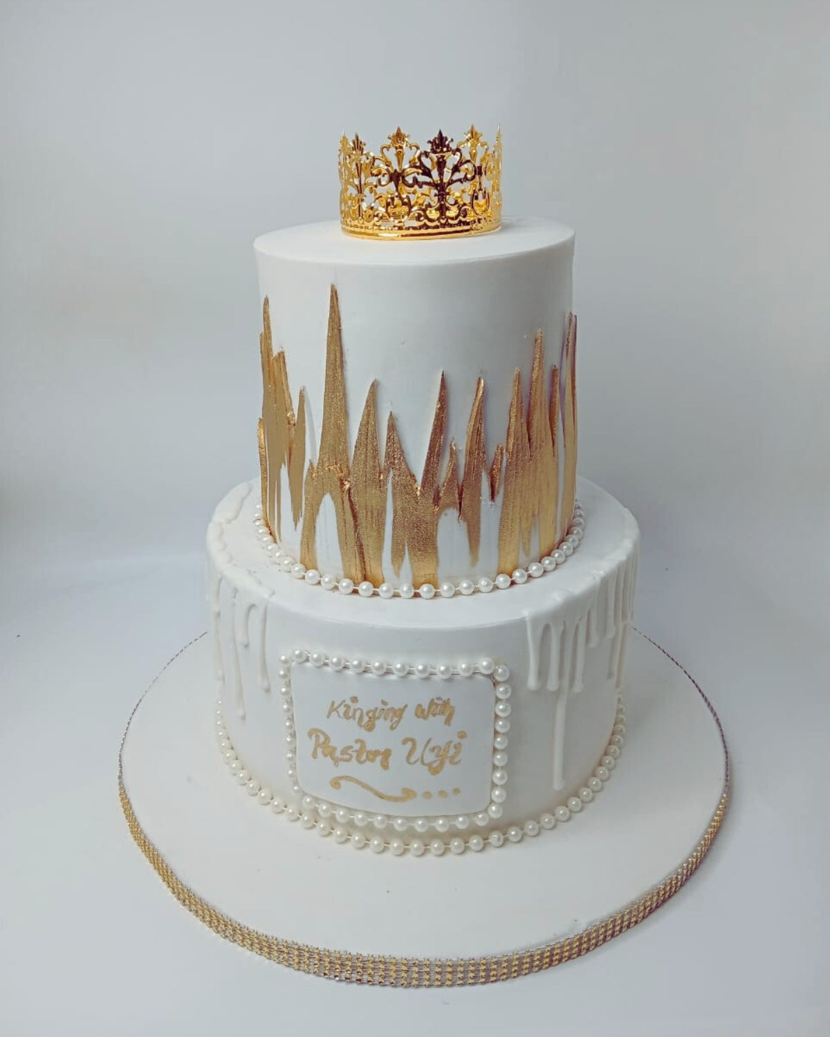 Two-tiered cake with gold decorations and a crown on a white background