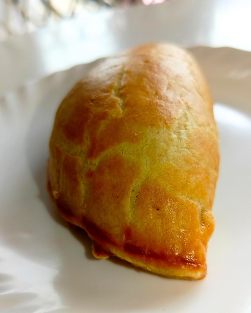 Fresh golden meat pie on a white plate with a blurred background