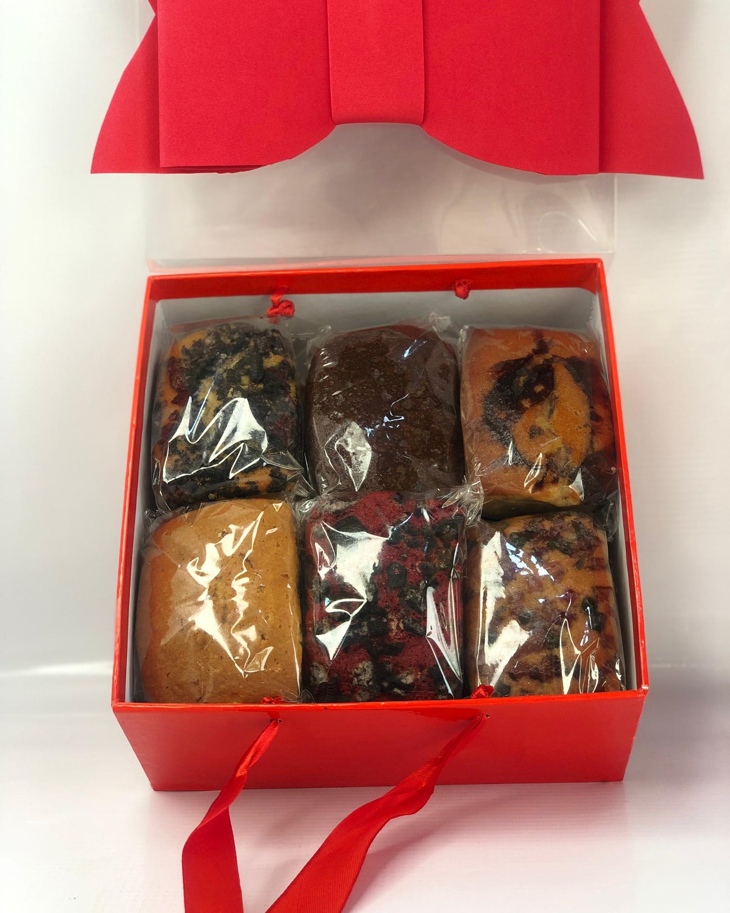 Red gift box with transparent lid containing wrapped mini loaves on a white background