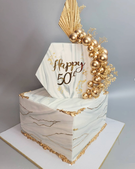 Decorative cake with gold accents and 'Happy 50th' text on a gray background