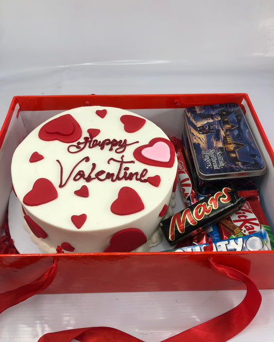 Valentine's Day cake with red hearts and 'Happy Valentine' text, surrounded by candy bars in a red box.