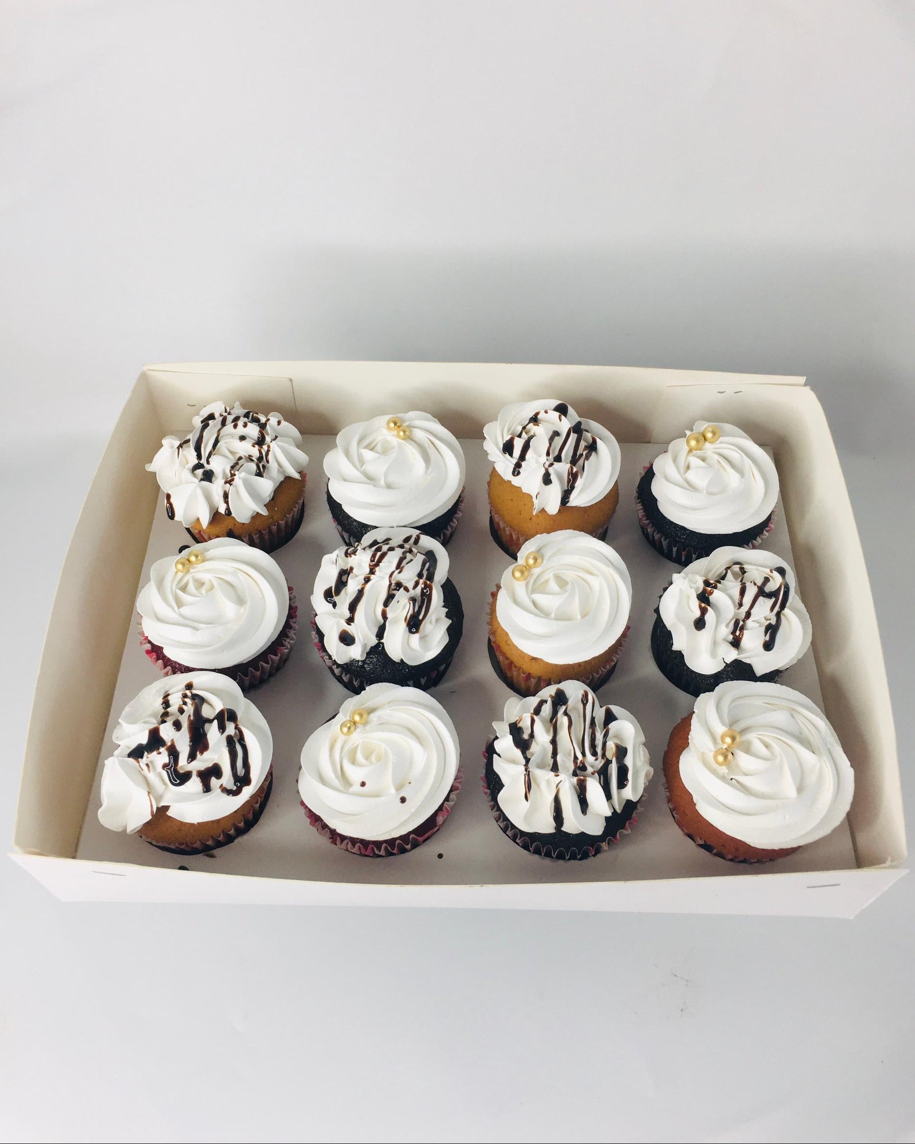 Box of cupcakes with white frosting and chocolate drizzle on a light gray background