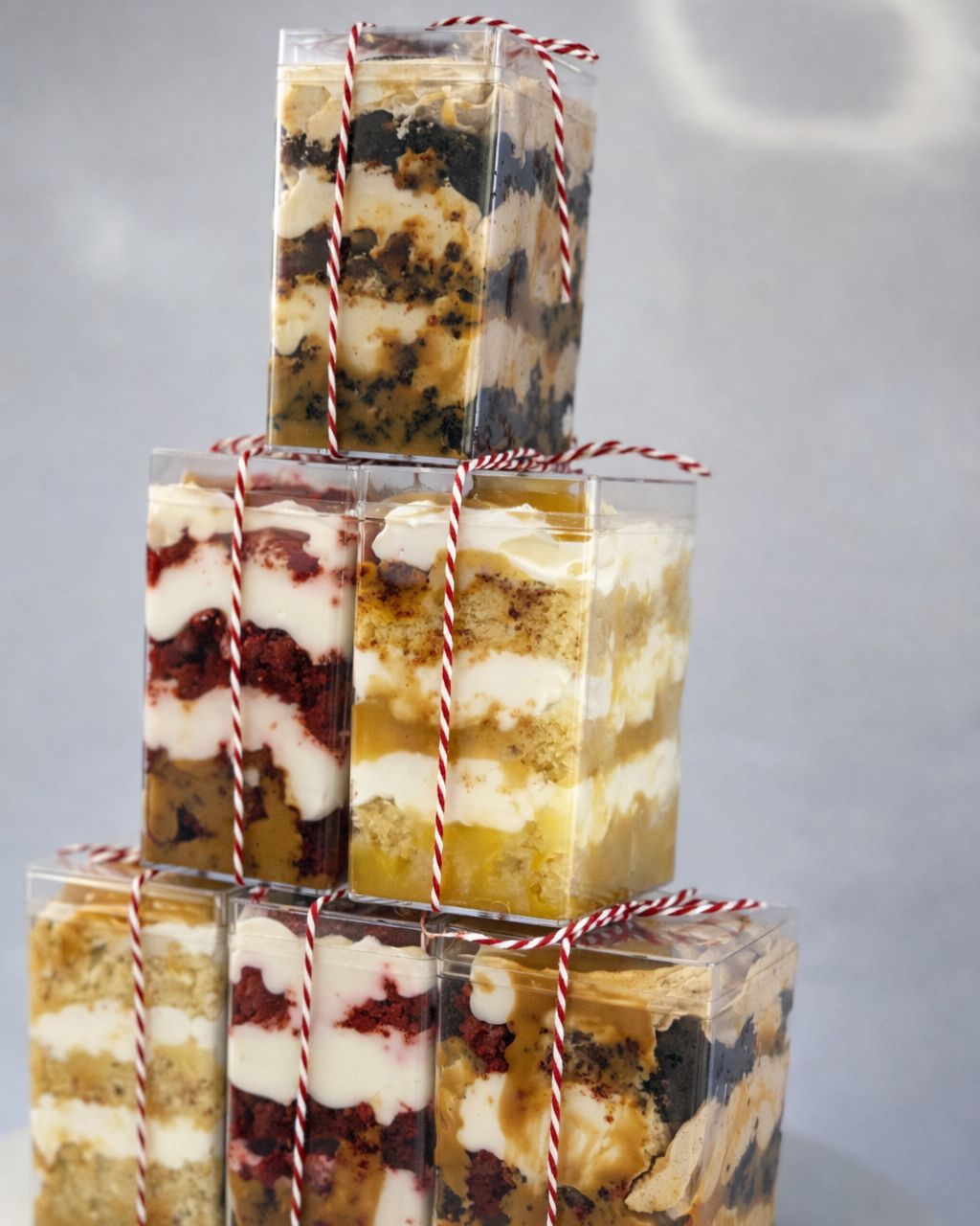 Stack of layered cake trifles (parfait) in clear packaging with red and white string on a gray background